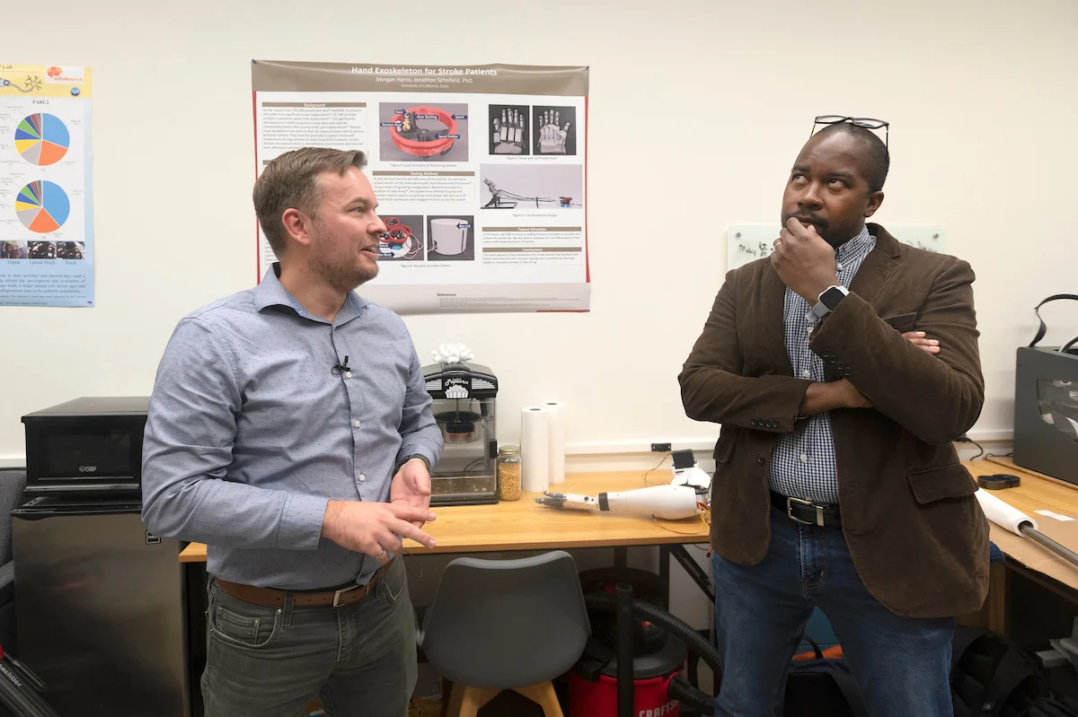 Jonathan Schofield talks to Wilsaan Joiner who has his hand on his chin, glasses on the top of his head and has a pensive look on his face.