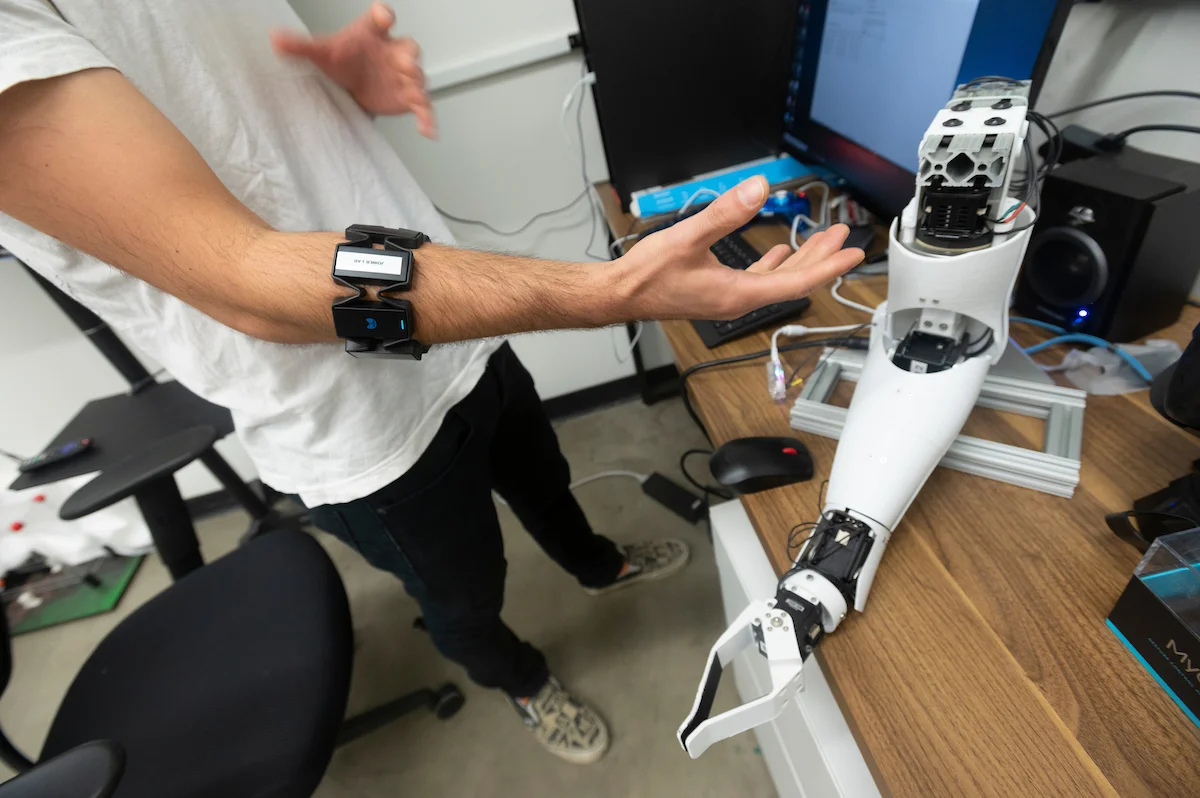 Close up of human arm with sensors on it next to white robotic arm.
