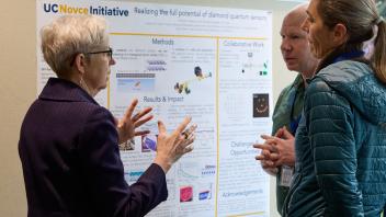 three people engaged in conversation near a research poster